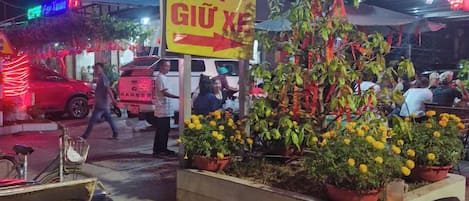 A street scene with a neon sign for a restaurant, a bicycle, and potted plants.
