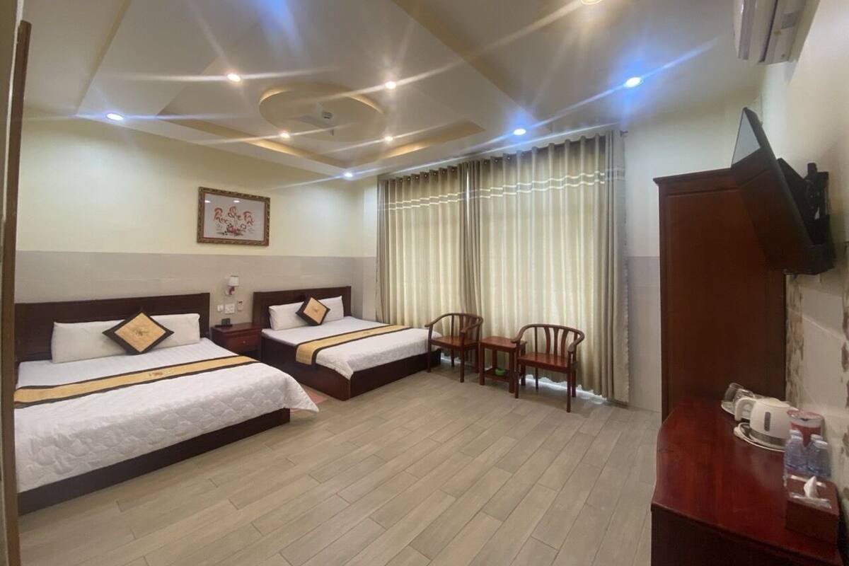 A hotel room with two beds, a desk, chairs, a TV, and a window with curtains.