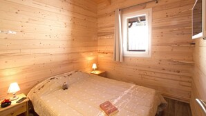 A cozy wooden cabin room with a bed, a nightstand, a lamp, and a window. - Chalet Privé,  proche de la Navette (Les Menuires)