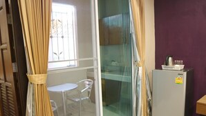A room with a sliding glass door leading to a balcony, a small table and chair, a refrigerator, and a purple wall. - BB Residence (Pattaya)