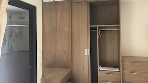 A bedroom with a wooden wardrobe, a small desk, and a shower area. - BB Residence (Pattaya)