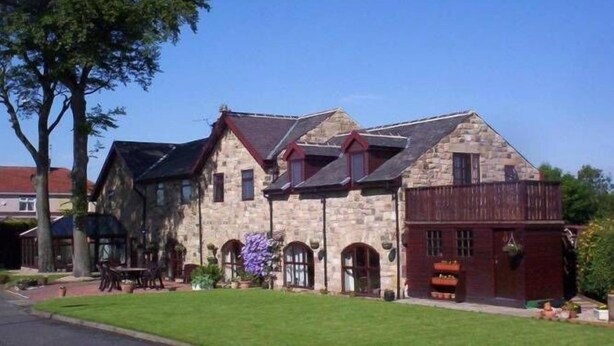 A stone building with a gabled roof and a wooden extension. - Stone Cottage (Newcastle-upon-Tyne)