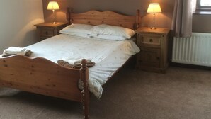 A bedroom with a wooden bed, two bedside tables with lamps, a radiator, and a window with curtains. - Stone Cottage (Newcastle-upon-Tyne)