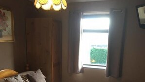 A bedroom with a bed, a wooden headboard, a window with curtains, and a hanging light fixture. - Stone Cottage (Newcastle-upon-Tyne)