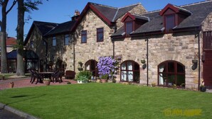 A stone building with a well-maintained lawn and outdoor seating area. - Stone Cottage (Newcastle-upon-Tyne)