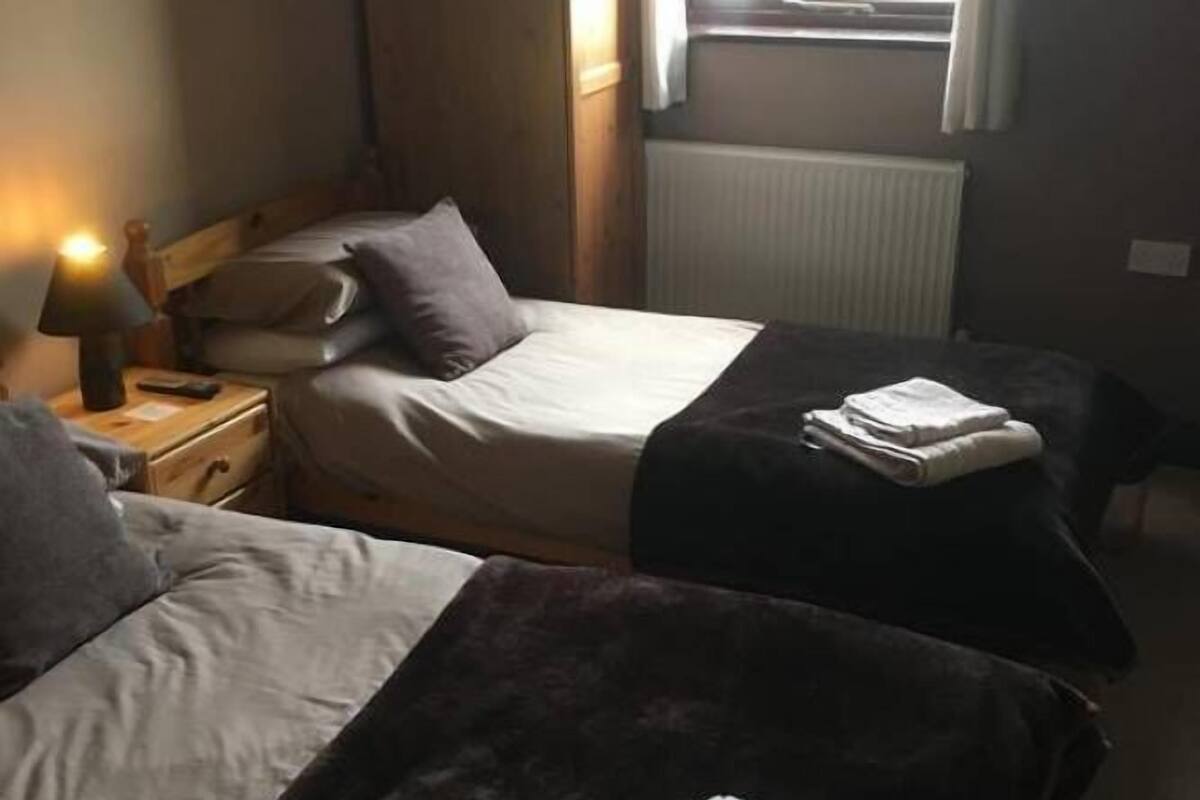 Une chambre avec deux lits, une table de chevet avec une lampe et une fenêtre avec des rideaux.