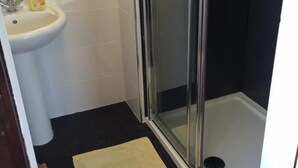 A bathroom with a glass-enclosed shower, a white sink, and a beige rug. - Stone Cottage (Newcastle-upon-Tyne)