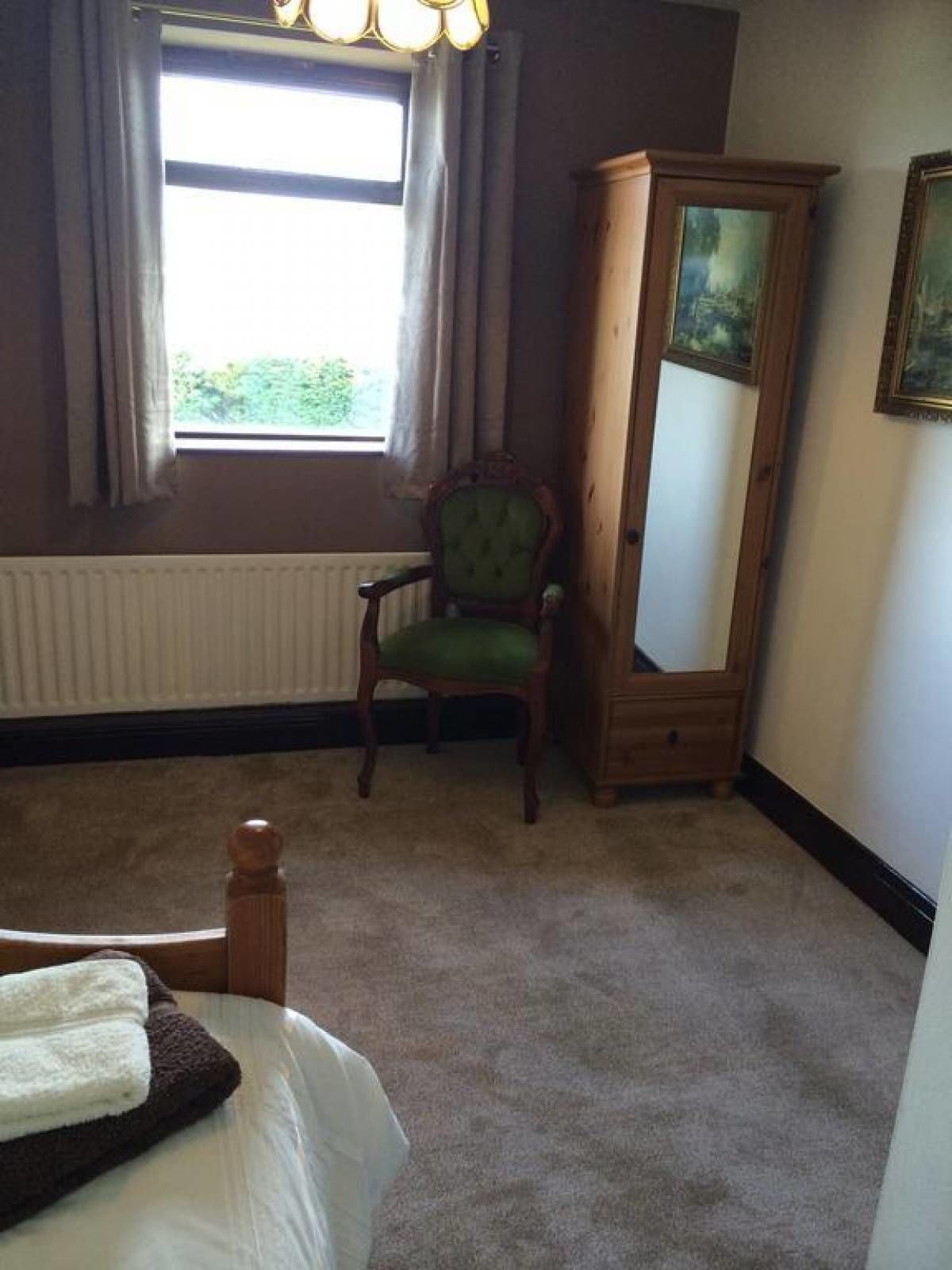 Une chambre à coucher avec un lit, une chaise, une armoire et une fenêtre avec des rideaux.