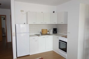 Une cuisine de taille réduite, avec des meubles blancs, un réfrigérateur, une machine à café et un four.