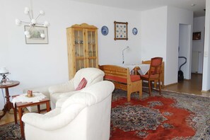 Un salon avec un canapé blanc, un meuble en bois, un tapis à motifs rouges et une chaise en bois.