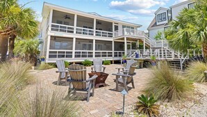 A two-story beachfront house with a balcony, outdoor seating area, and a view of the ocean. - Oceanfront Ground Level Duplex, Beach Boardwalk, Screened Porch, Dog Friendly (Pawleys Island)