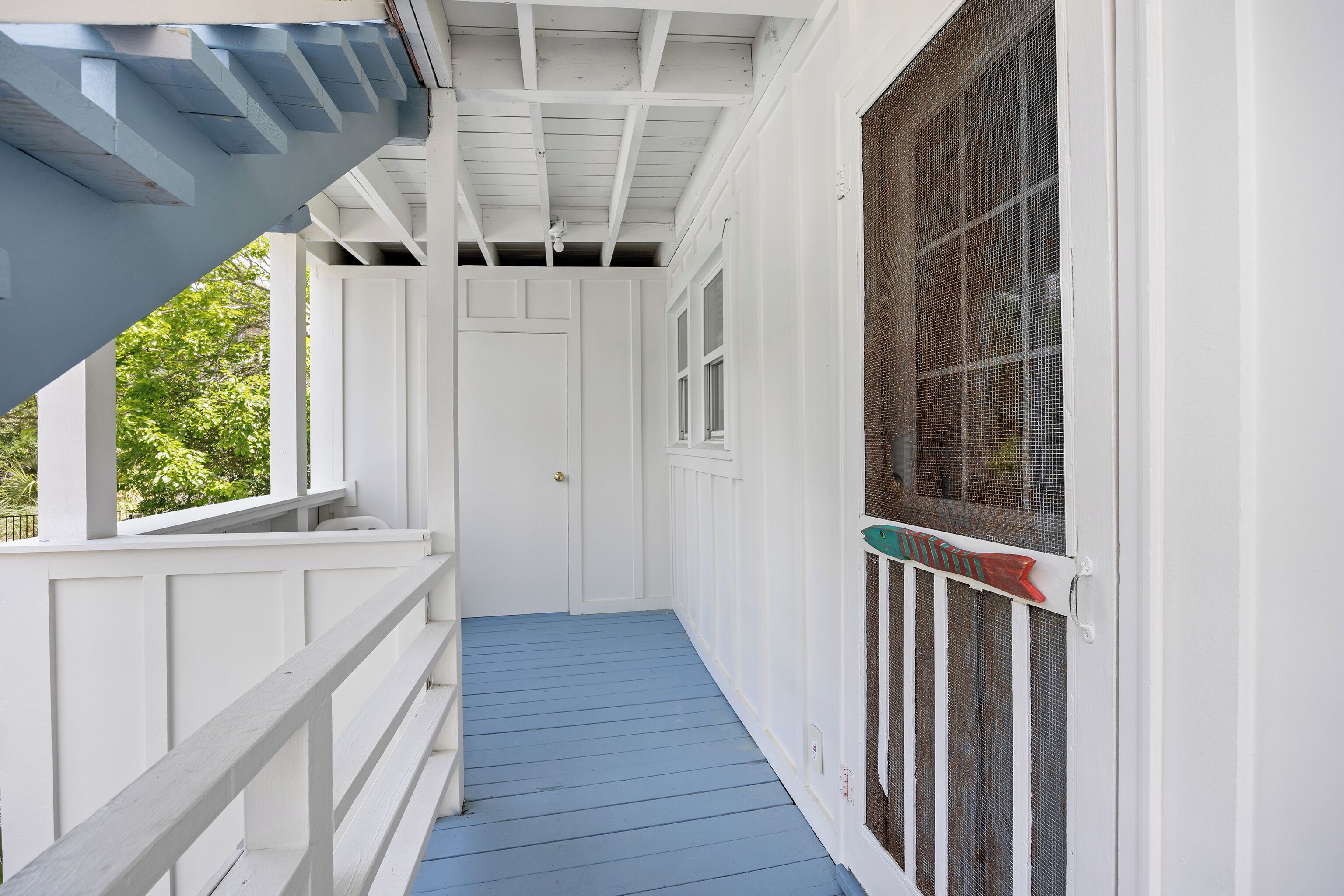 A covered porch with a blue floor, white railings, and a mesh screen door.