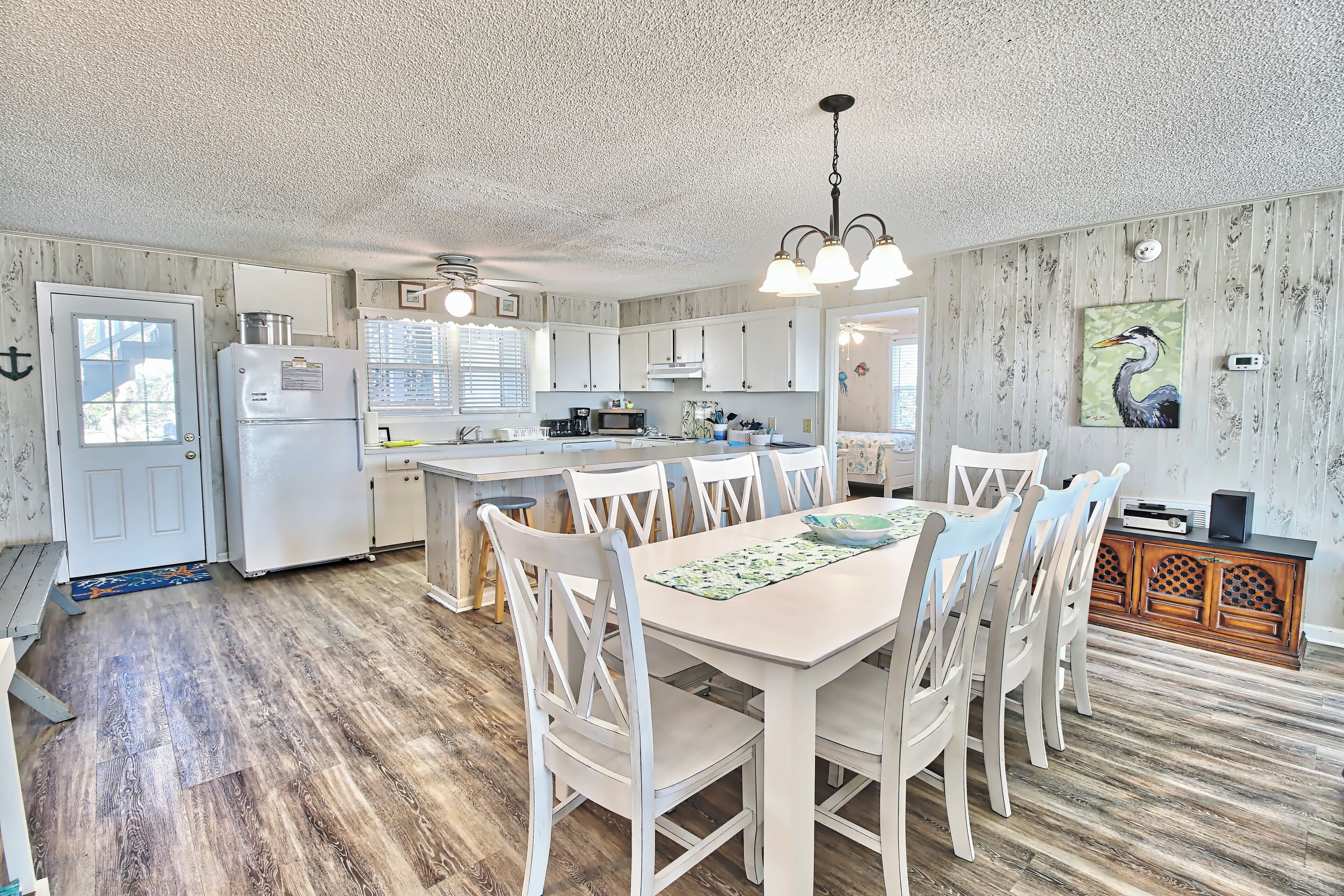 A spacious kitchen with white cabinets, a central island, and a dining area with white chairs.