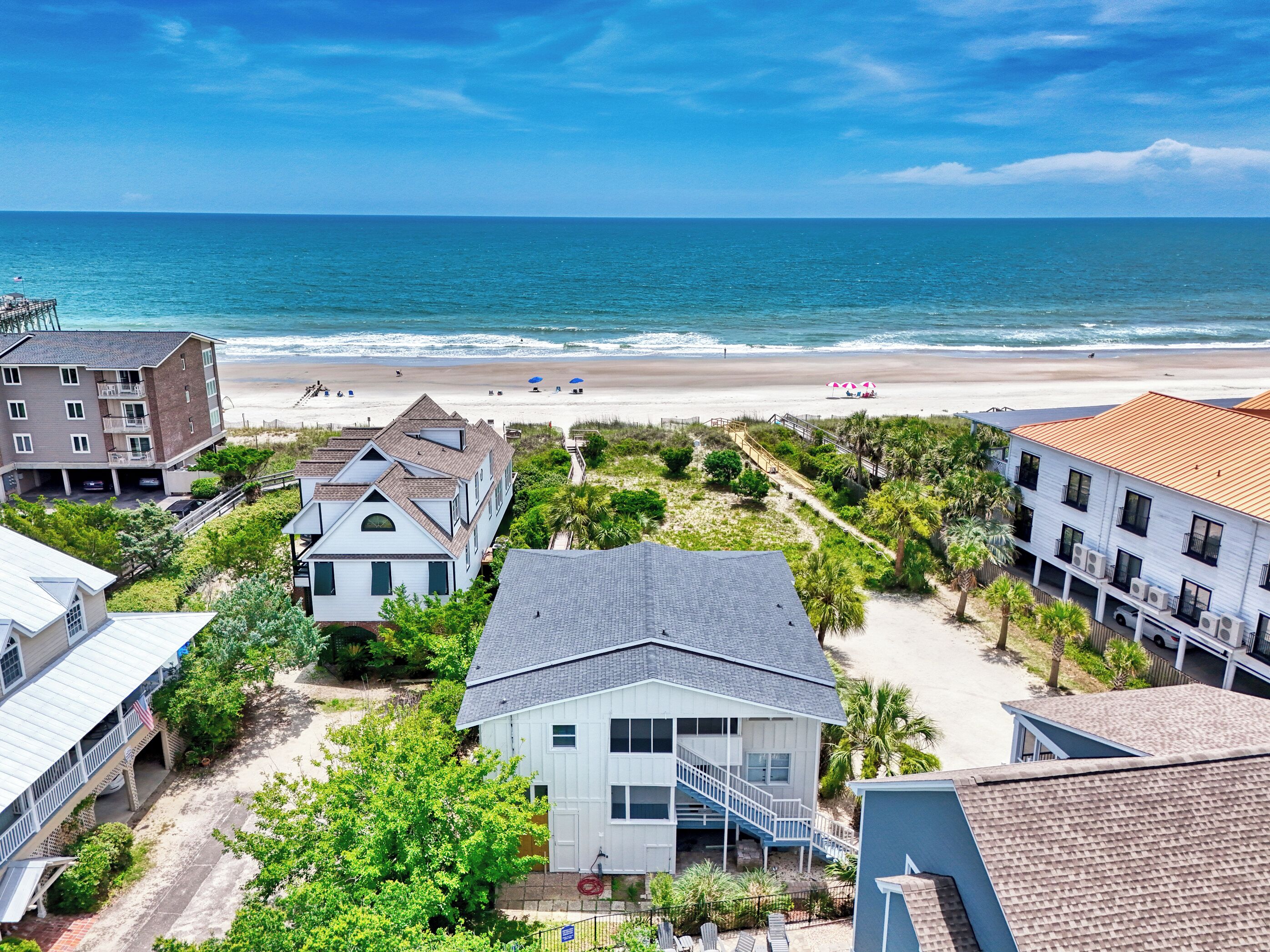A coastal residential area with beachfront properties, including a house with a staircase leading to a deck and a building with a red roof.