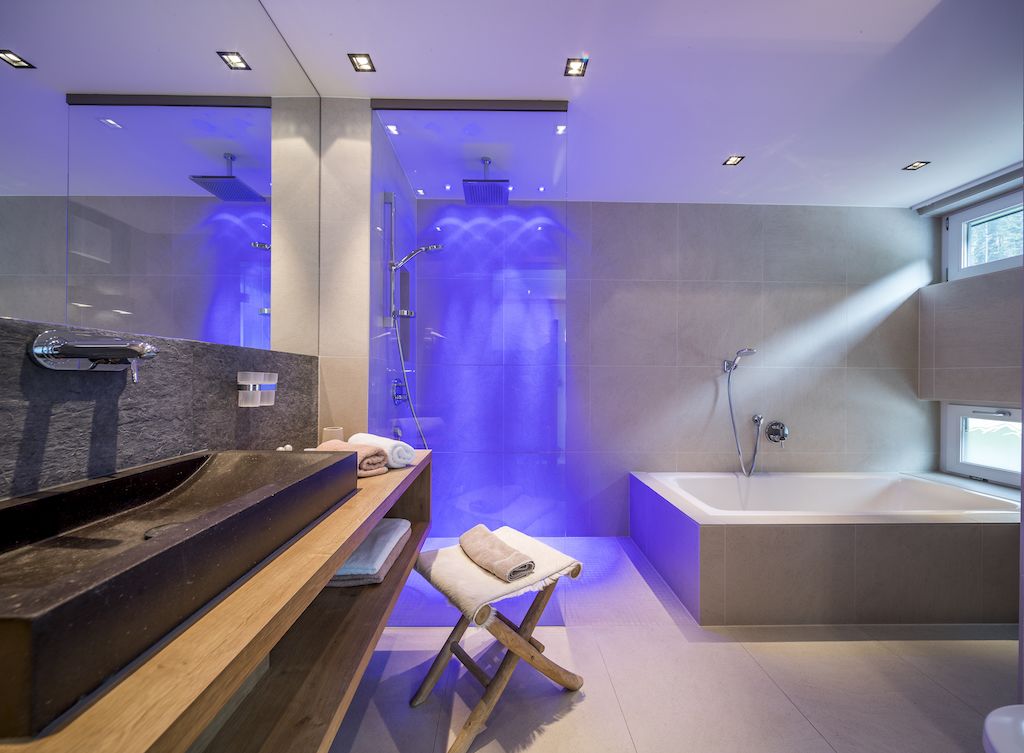 A modern bathroom with a wooden vanity, a bathtub, and a shower with blue lighting.