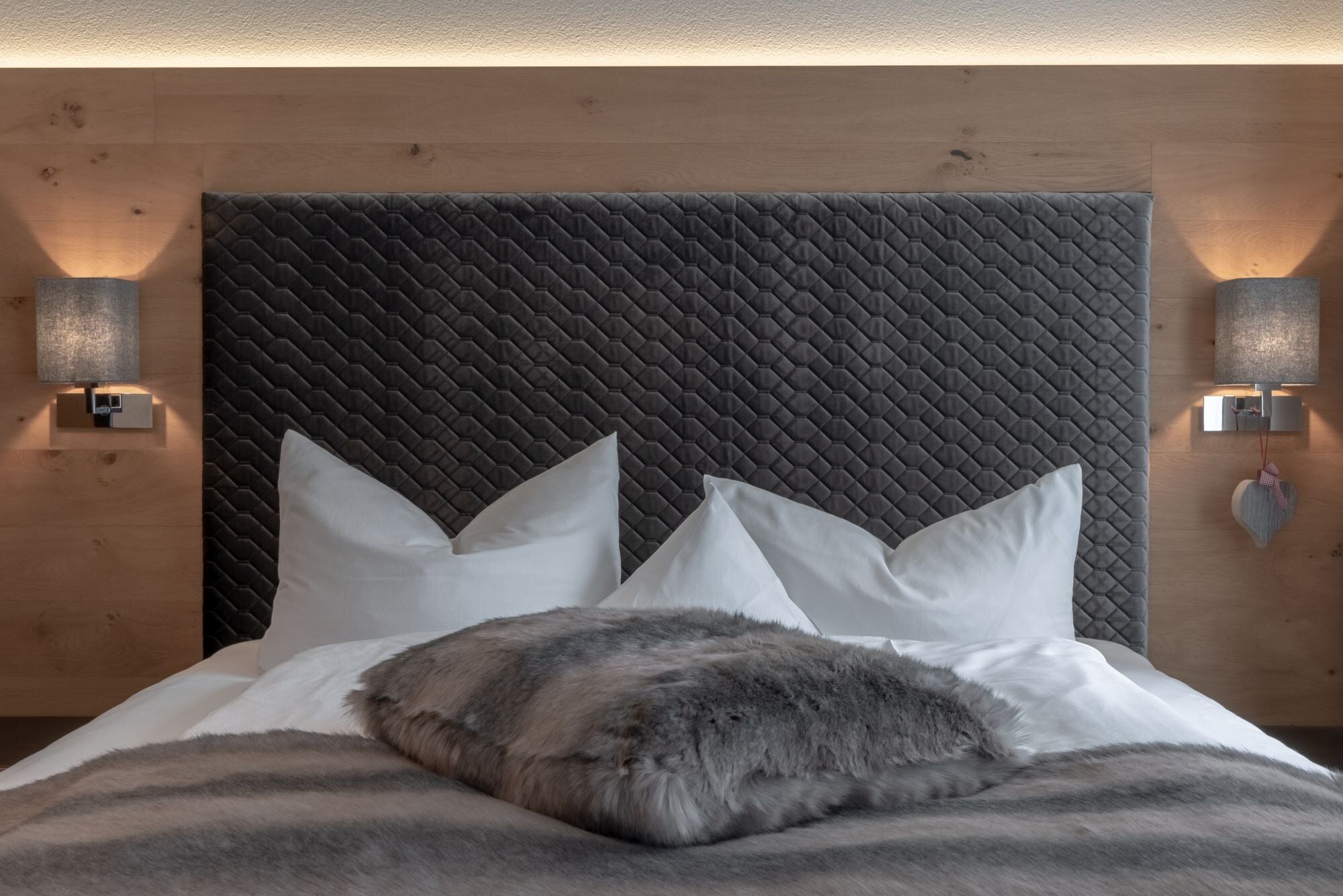 Ein modernes Schlafzimmer mit gestepptem Kopfteil, weißer Bettwäsche und zwei Wandleuchten.
