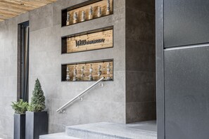 A modern building entrance with a 'Willkommen' sign, a wooden shelf with decorative items, and a metal handrail. - Post Hotel (See)