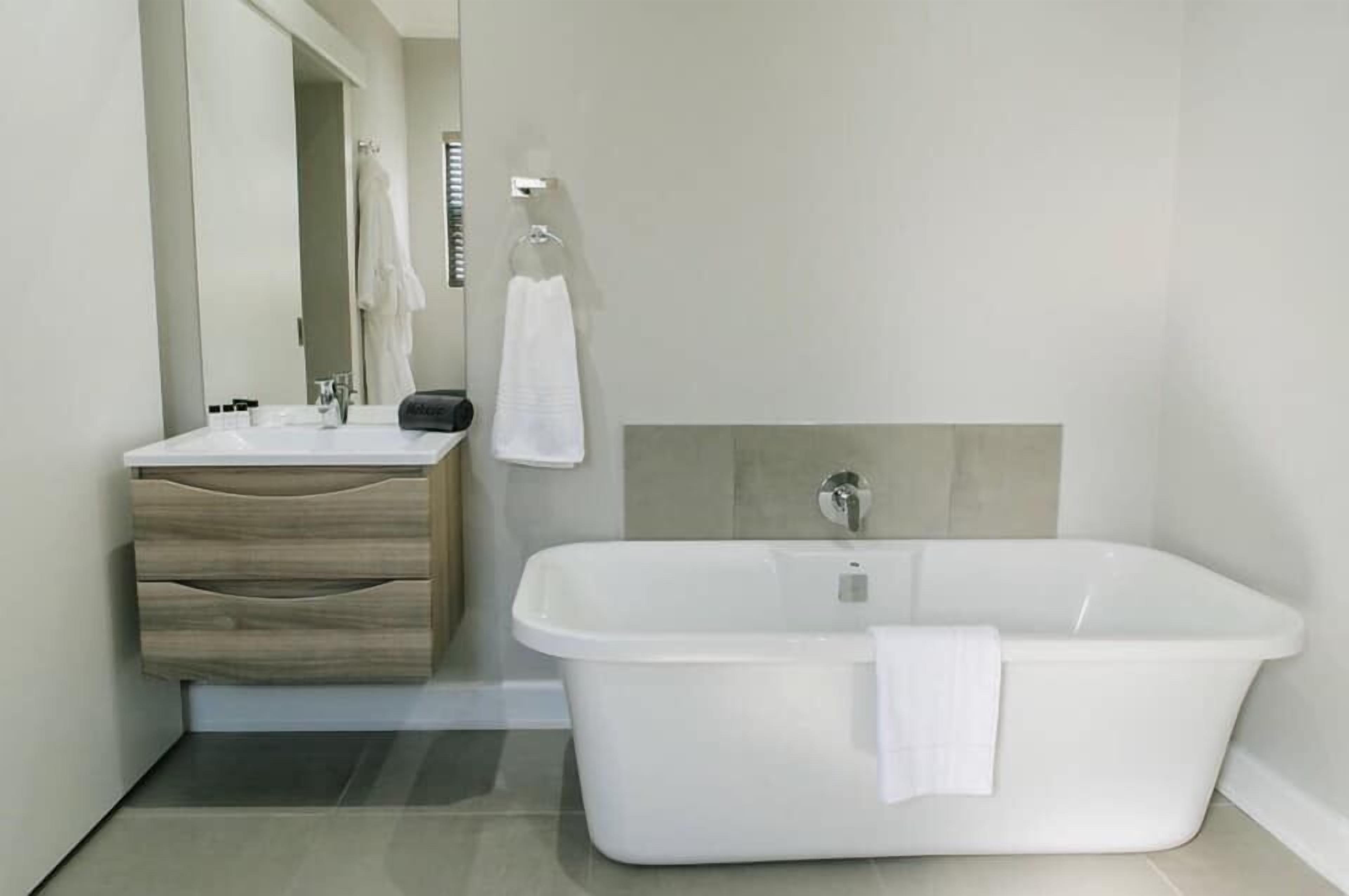 A modern bathroom with a white bathtub, a wooden vanity with drawers, and a large mirror.
