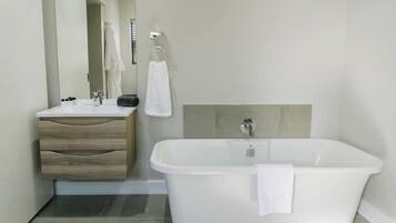 A modern bathroom with a white bathtub, a wooden vanity with drawers, and a large mirror.