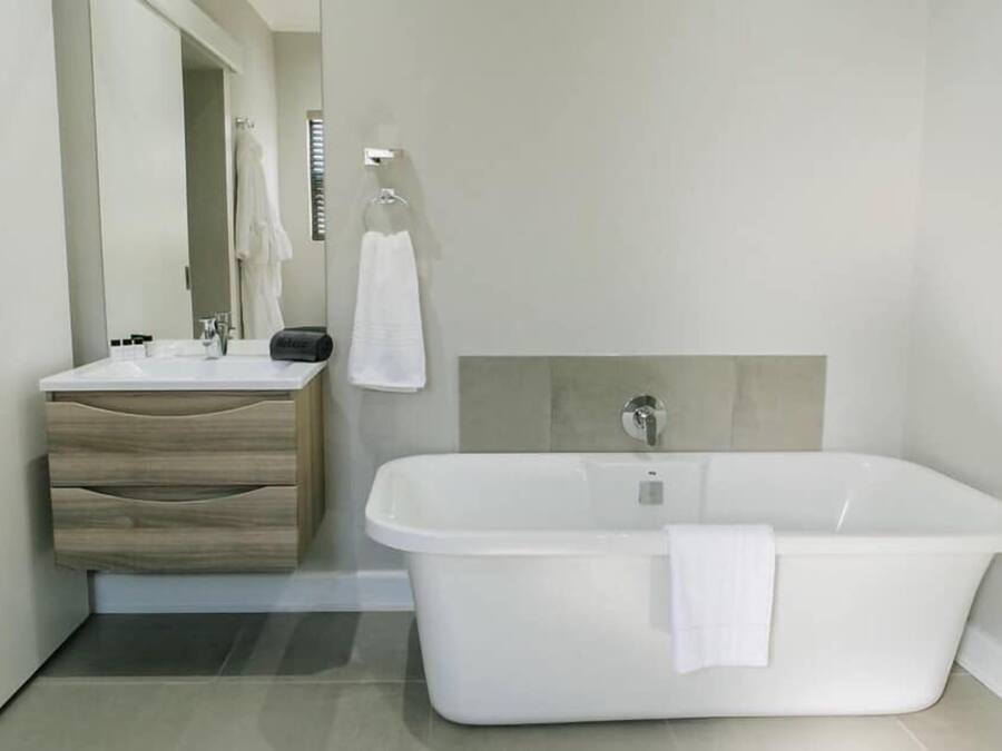 A modern bathroom with a white bathtub, a wooden vanity with drawers, and a large mirror.
