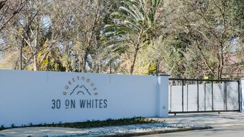 A white wall with the text "GUESTHOUSE 30 ON WHITES" and a palm tree in the background.