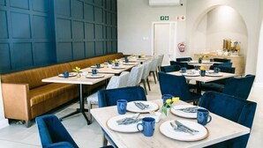 Un restaurant avec plusieurs tables et chaises, un banc et un espace cuisine à l’arrière-plan.