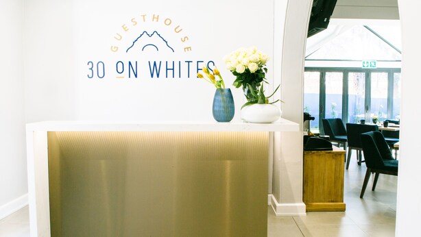 Un comptoir d’accueil avec une enseigne indiquant « Guesthouse 30 on Whites », et une vue sur la salle à manger, avec ses chaises et ses tables.