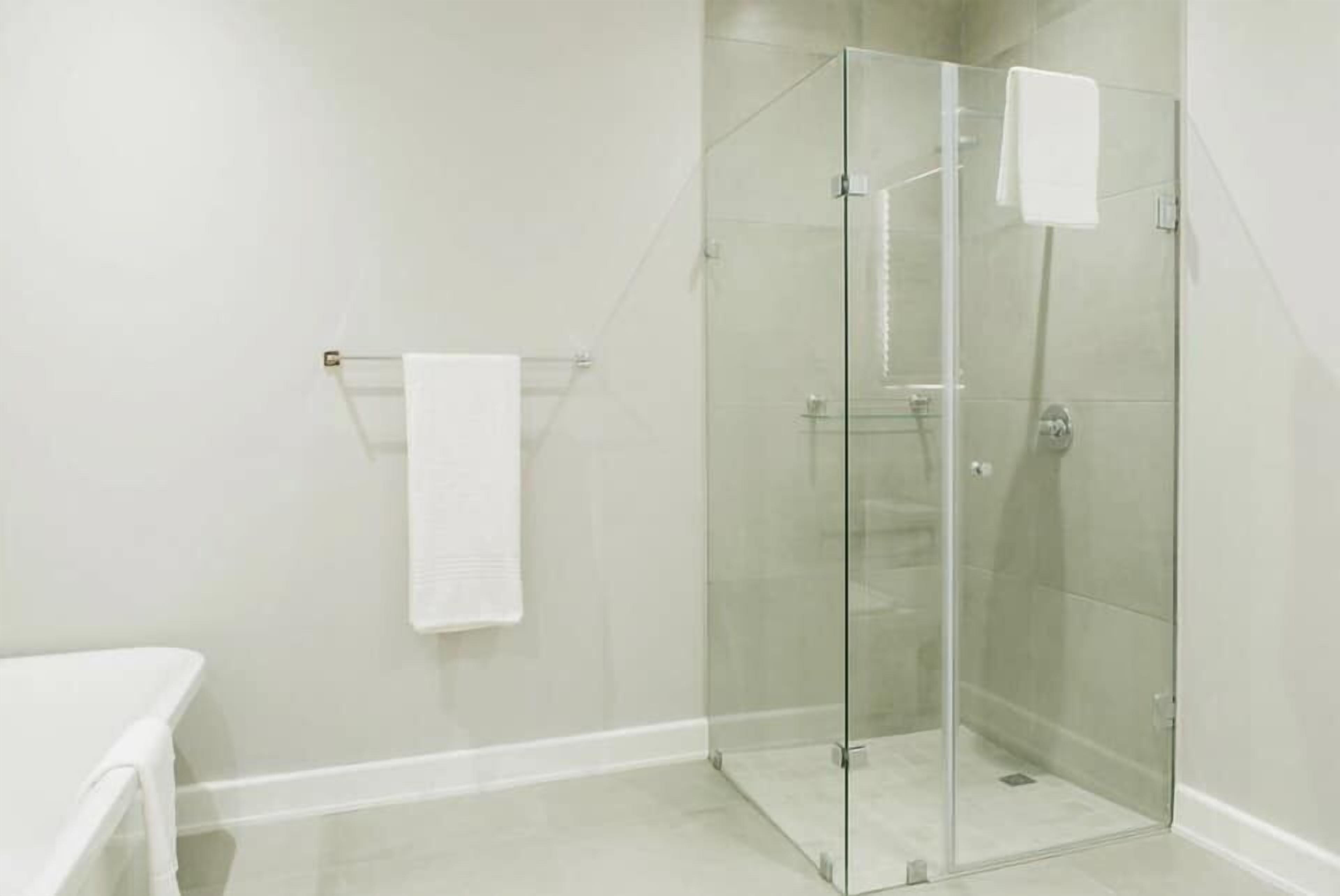 Une douche fermée par des parois de verre, avec une serviette blanche posée sur un porte-serviettes, un banc blanc et un sol carrelé.