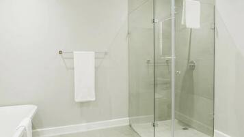 Une douche fermée par des parois de verre, avec une serviette blanche posée sur un porte-serviettes, un banc blanc et un sol carrelé.