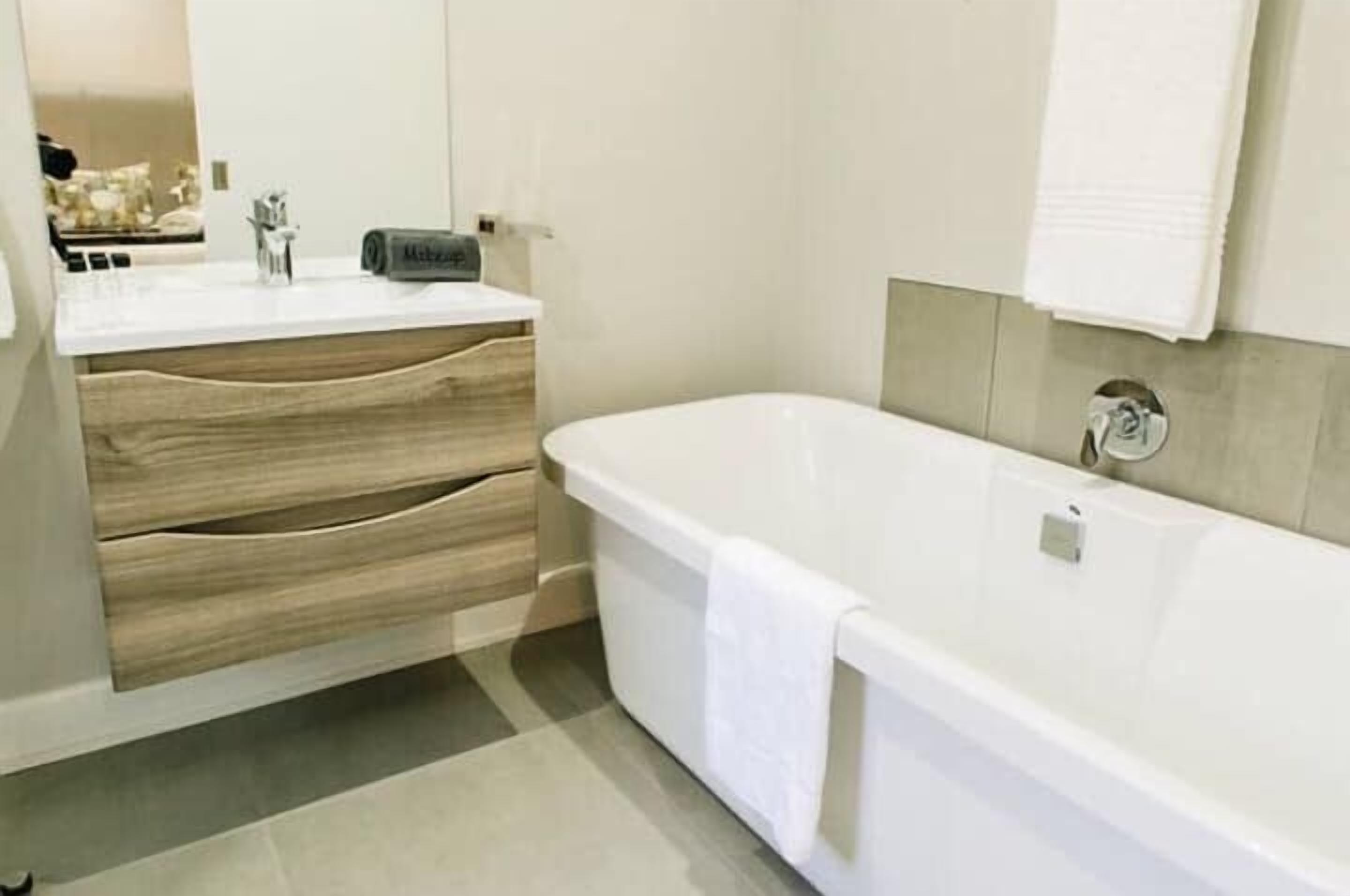 A modern bathroom with a white bathtub, wooden vanity with drawers, and a large mirror.