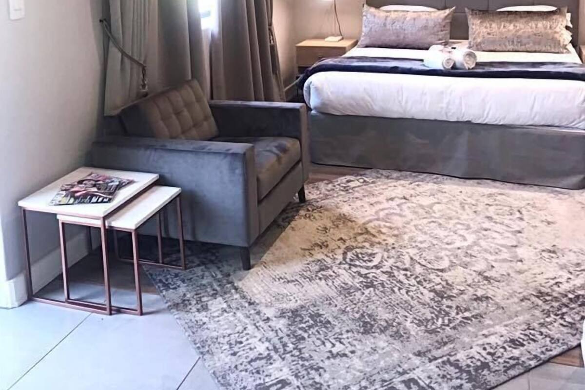 Un dormitorio con cama, una silla, una mesita, una lámpara y un reloj grande en la pared.