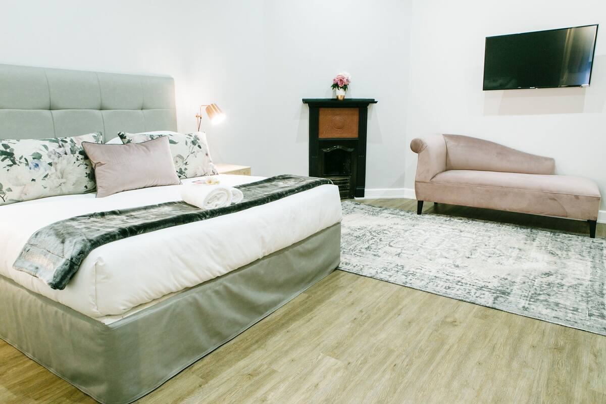 Un dormitorio ordenado con cama, sofá, chimenea y televisor instalado en la pared.