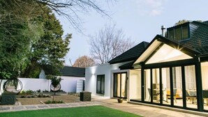 Une maison moderne dotée d’un patio couvert, d’une pelouse bien entretenue et d’un grand arbre en arrière-plan.