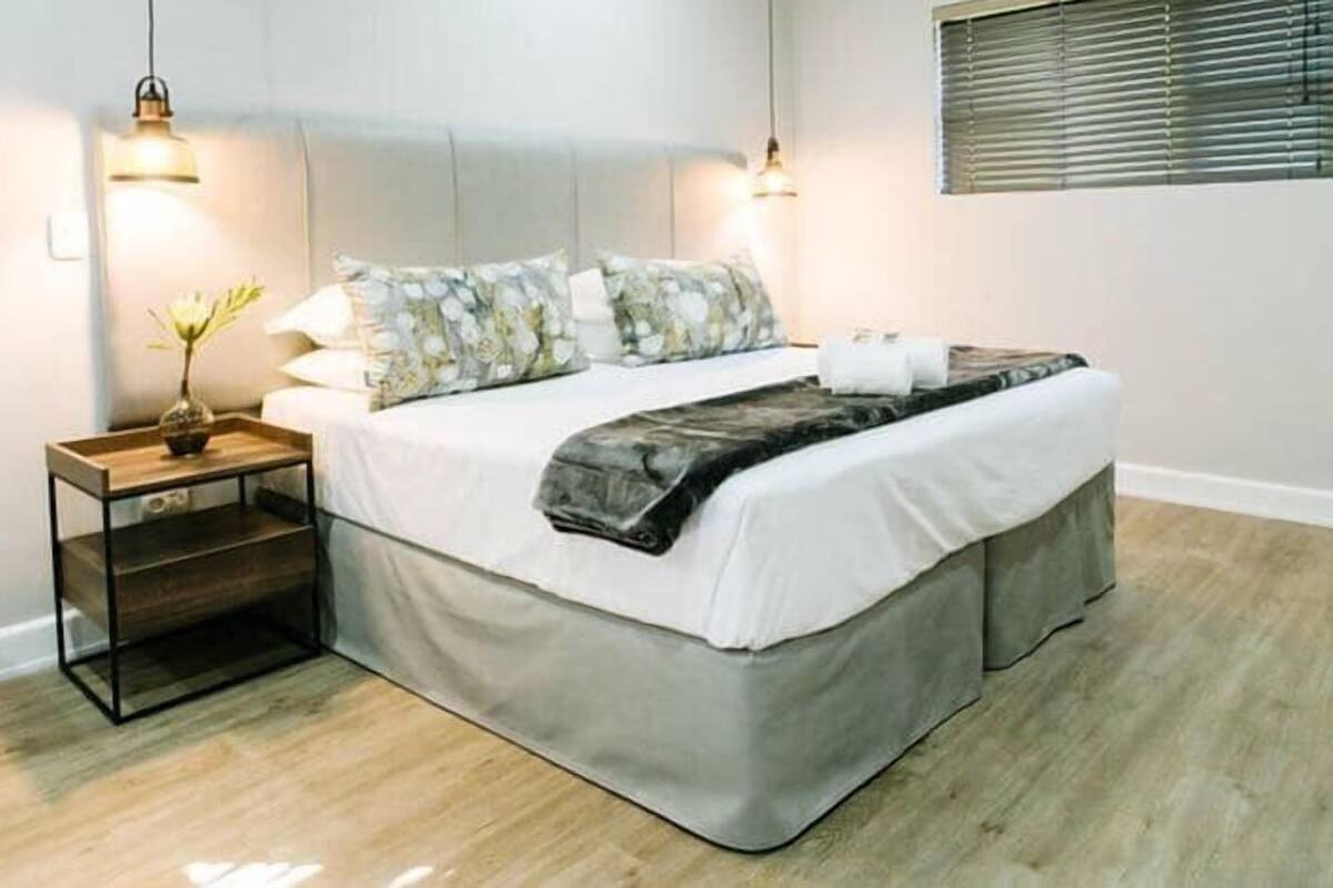 Un dormitorio ordenado con cama, mesitas de noche y una ventana con persianas.