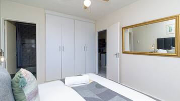 Un dormitorio con cama, ventilador de techo, espejo grande y armario.