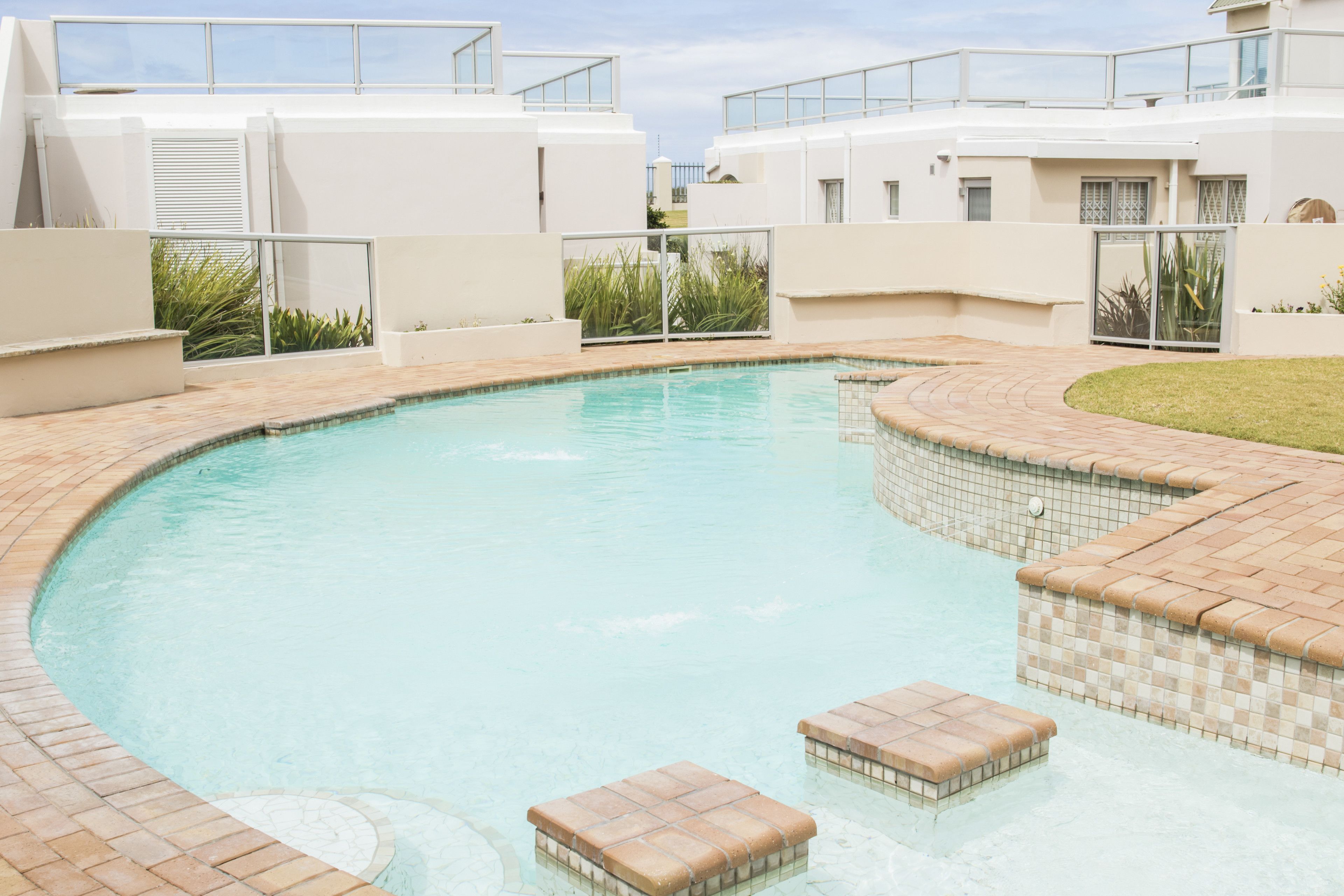 A swimming pool with tiled edges and steps, surrounded by a white building with balconies.