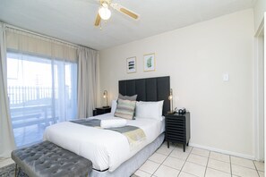 Une chambre d’hôtel avec un lit, une banquette, un ventilateur de plafond, une table de chevet et une fenêtre avec des rideaux.