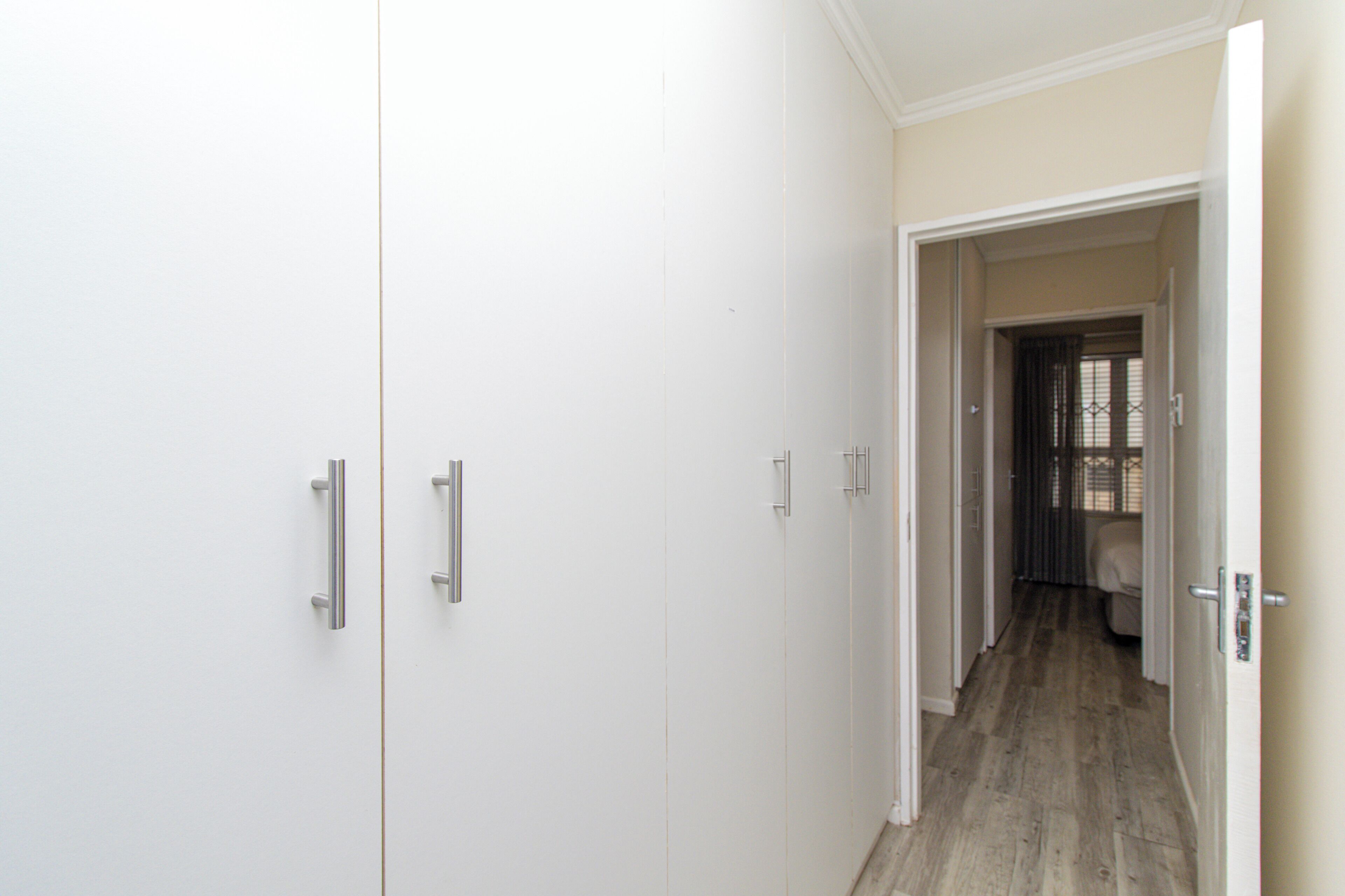 A hallway with white wardrobes and a door leading to a room with a bed.