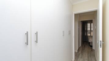 A hallway with white wardrobes and a door leading to a room with a bed.