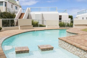Uma piscina com escadas em mosaico e um edifício moderno com guarda-corpo de vidro ao fundo.