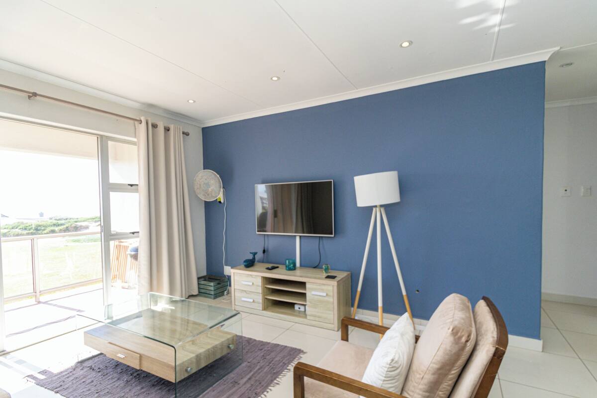 A modern living room with a glass coffee table, a sofa, a TV, and a floor lamp.