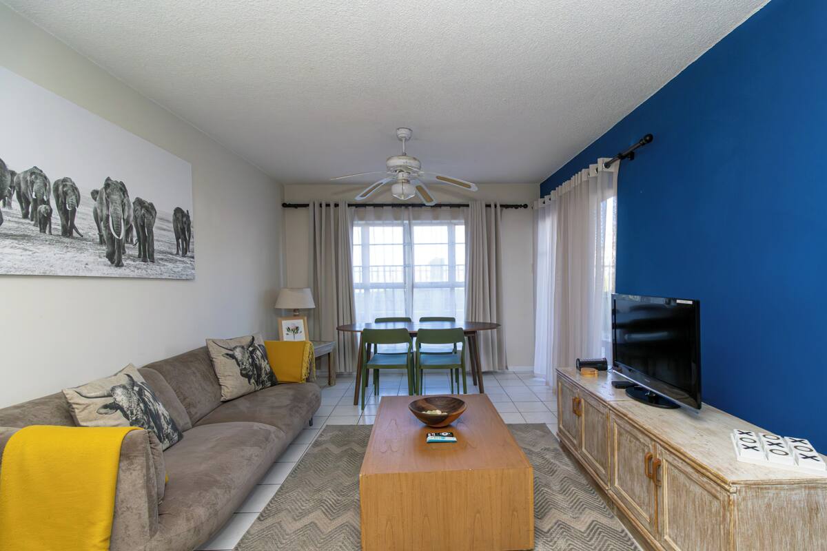 A living room with a sofa, a coffee table, a TV, a ceiling fan, a dining table with chairs, and a painting on the wall.