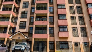 Un edificio residencial de varios pisos con balcones, ventanas amplias y un coche estacionado enfrente.