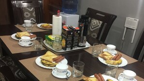 Una mesa de comedor dispuesta con platos de comida, incluyendo tostadas y bananas, además de diferentes condimentos y bebidas.