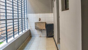 Un estrecho pasillo con suelo de baldosas, una ventana con rejas de metal, un lavamanos y un mueble pequeño.