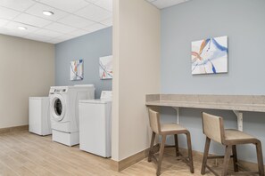 A laundry room with a washing machine, dryer, and two chairs. - Candlewood Suites Newnan - Atlanta SW by IHG (Newnan)