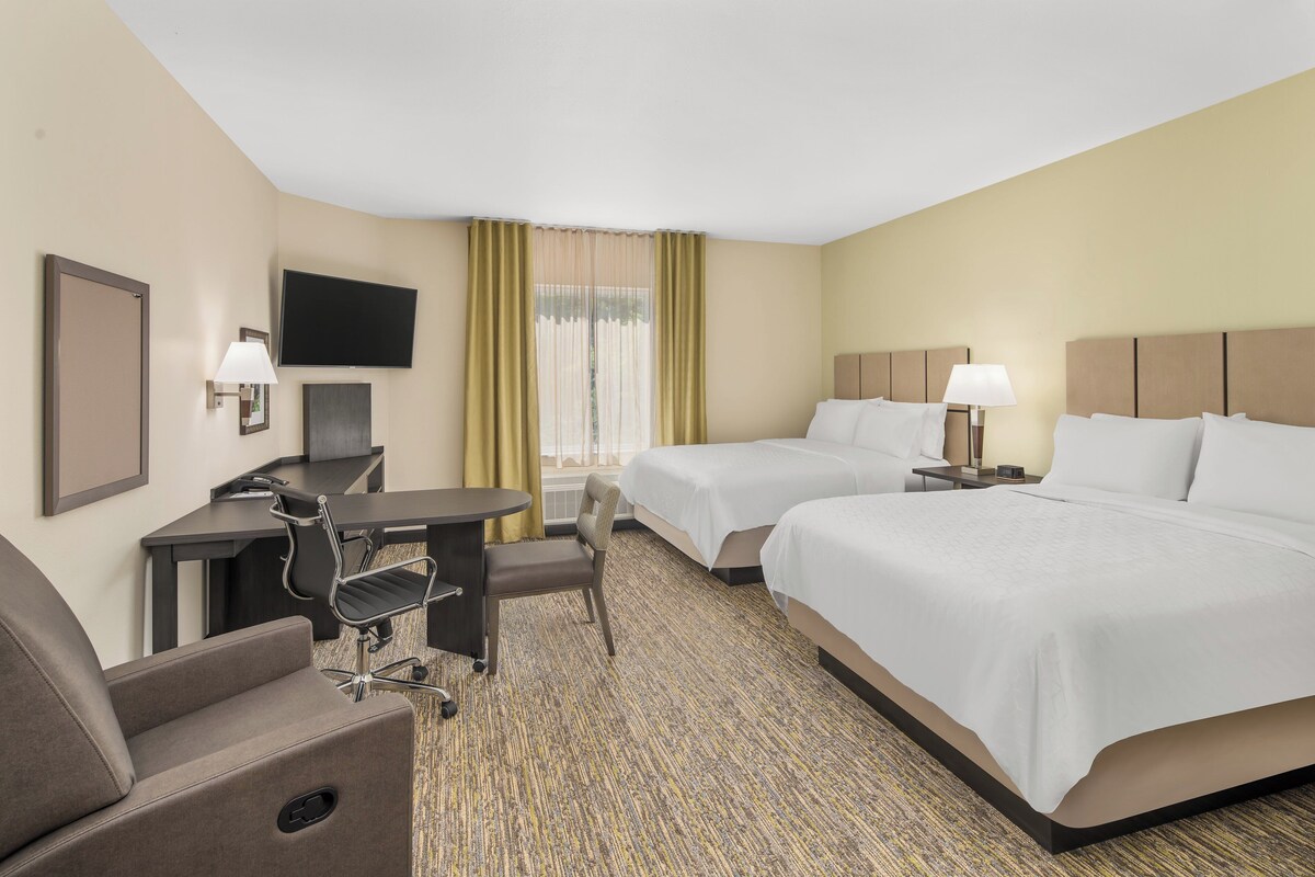 A hotel room with two beds, a desk, a chair, a TV, and a window with curtains.