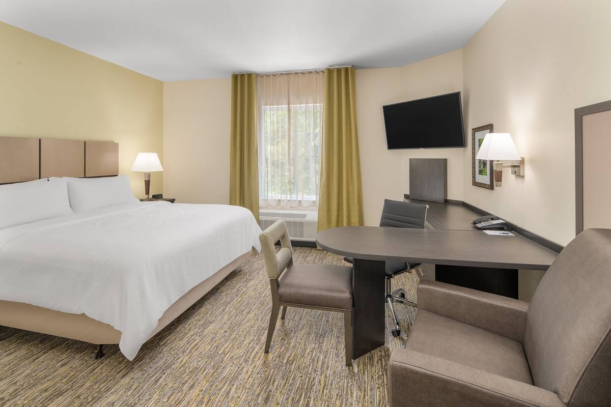 Une chambre d’hôtel équipée d’un lit, d’un bureau, d’une chaise, d’une télévision et d’une fenêtre avec des rideaux.