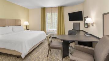 A hotel room with a bed, a desk, a chair, a TV, and a window with curtains.