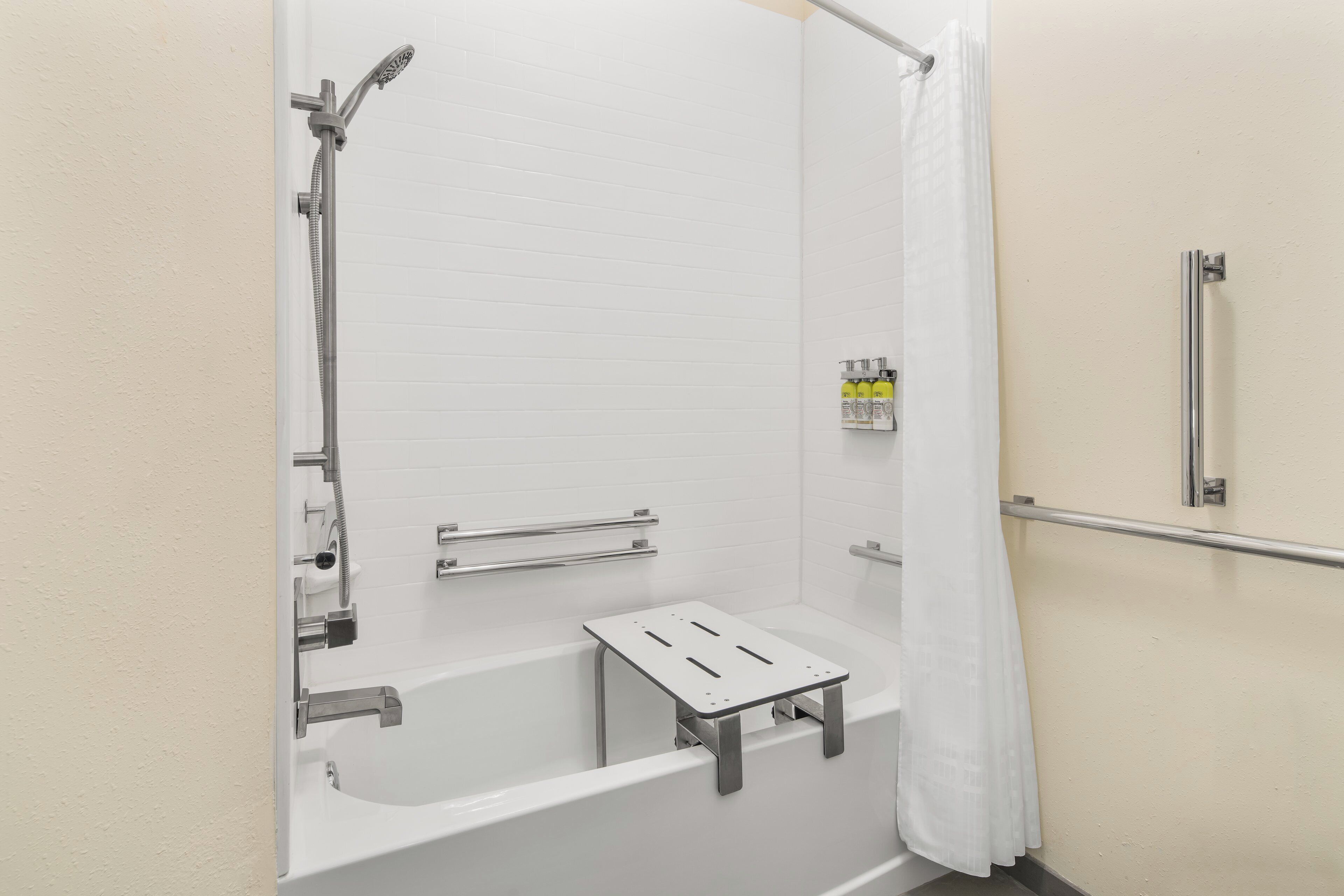 Cabina de ducha blanca con cabezal de ducha de mano, rociador de mano y barra de apoyo.